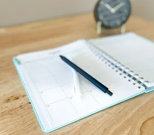 Agenda abierta por un calendario mensual con dos bolígrafos, sobre una mesa de madera