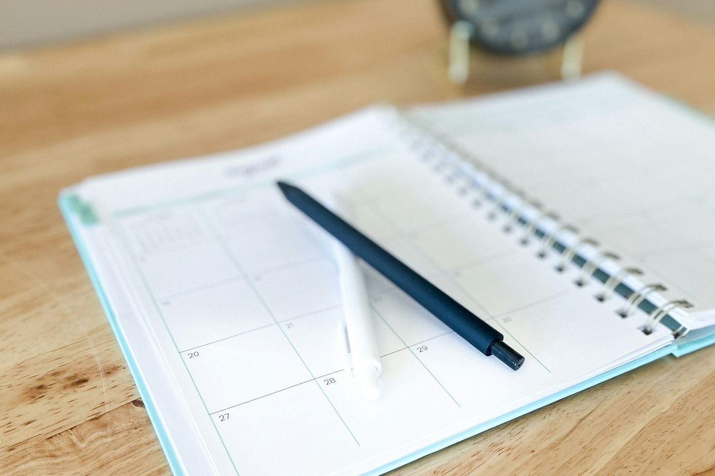 Agenda abierta por un calendario mensual con dos bolígrafos, sobre una mesa de madera
