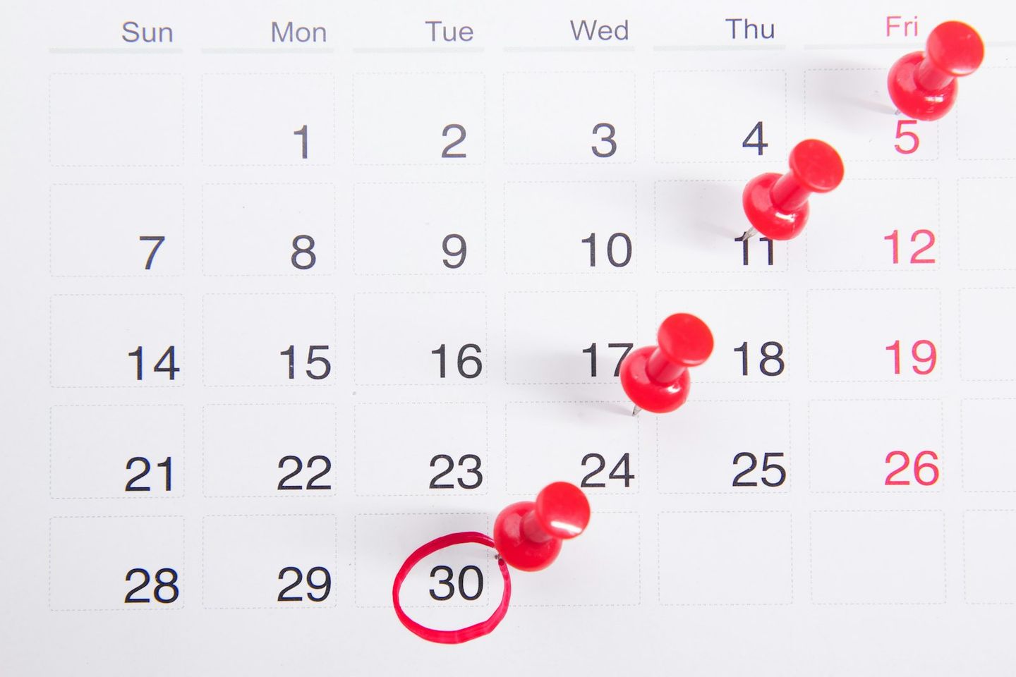Calendario mensual con chinchetas rojas clavadas en varios días y el día 30 rodeado con un círculo rojo
