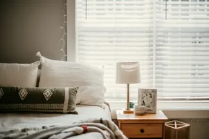 Dormitorio tranquilo con cojines blancos, una lámpara en la mesilla y luz natural que entra por la persiana
