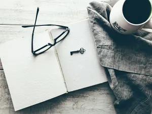 Unas gafas y una llave antigua sobre un cuaderno abierto, junto a una taza de café