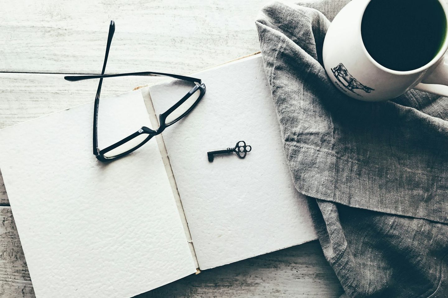 Unas gafas y una llave antigua sobre un cuaderno abierto, junto a una taza de café