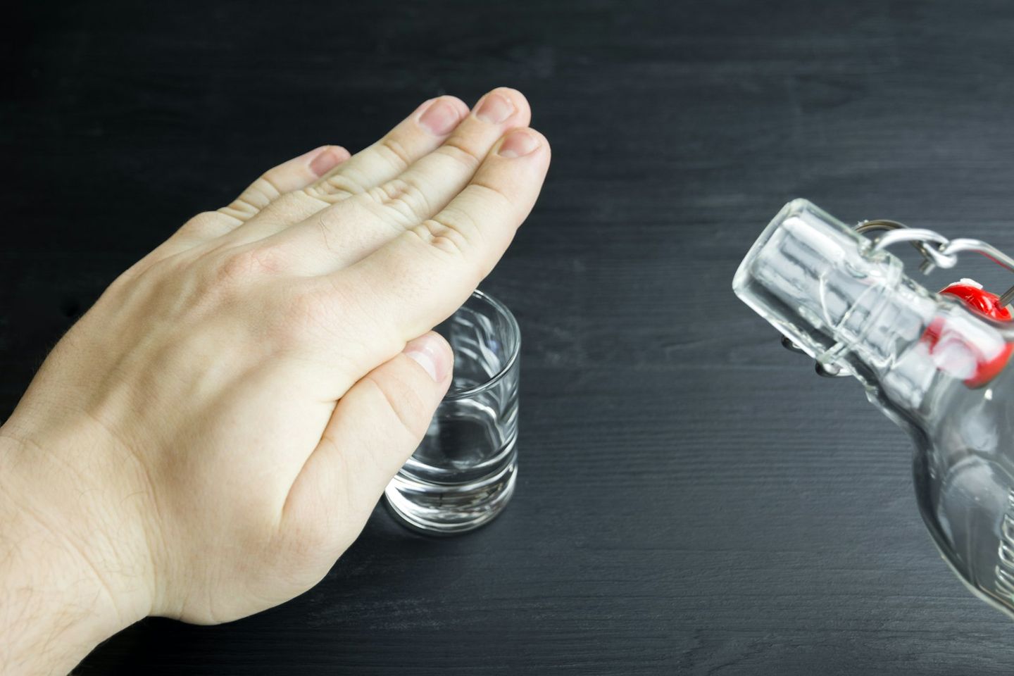 Una mano tapa un vaso pequeño para rechazar la bebida de una botella de cristal
