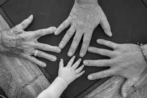 Manos de cuatro personas de distintas edades, de un bebé a una persona mayor, apoyadas juntas sobre una mesa