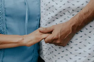 Dos personas cogidas de la mano, una con blusa azul y otra con camisa estampada