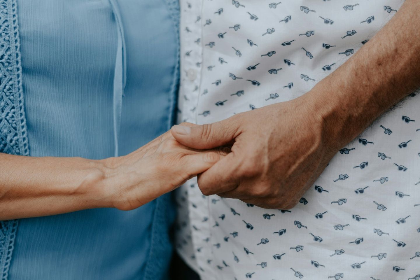 Dos personas cogidas de la mano, una con blusa azul y otra con camisa estampada