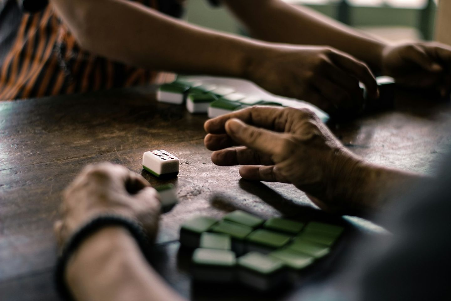 Manos de varias personas jugando al dominó sobre una mesa de madera