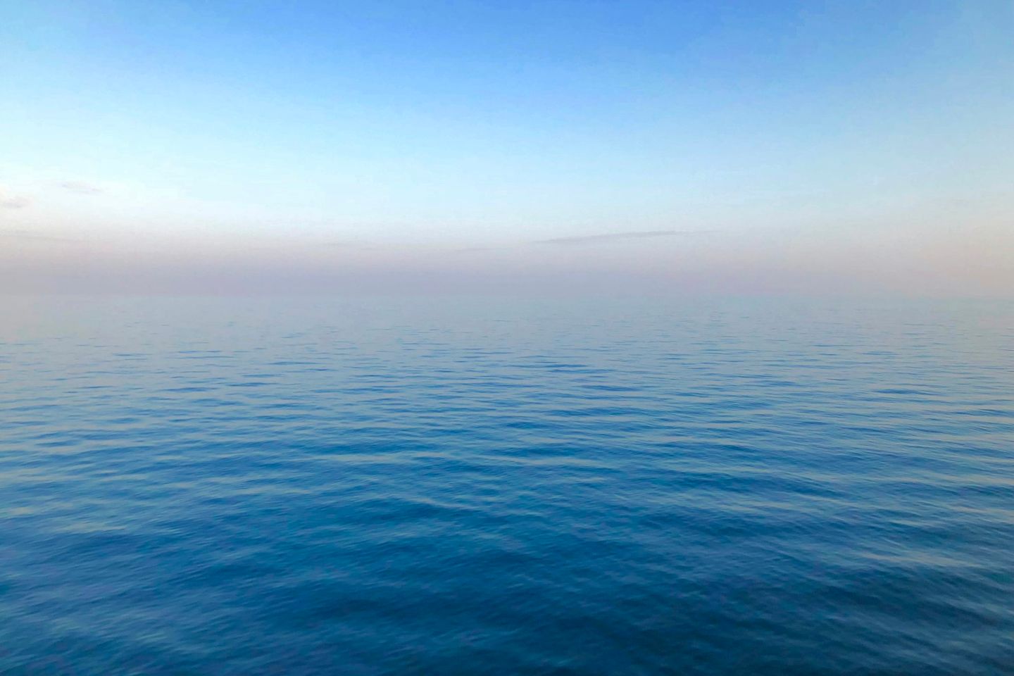Mar en calma con un horizonte recto, bajo un cielo azul que se aclara hacia el horizonte