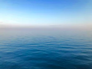 Mar en calma con un horizonte recto, bajo un cielo azul que se aclara hacia el horizonte