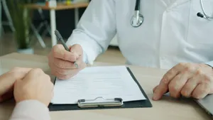Manos de un médico con bata y estetoscopio que toma notas en una consulta, frente a las manos de un paciente
