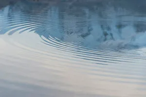 Ondas concéntricas que se extienden sobre la superficie de un agua en calma, con reflejos azules y grises