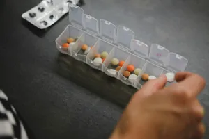 Mano cogiendo una pastilla de un pastillero semanal con varios compartimentos