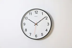 Reloj de pared con esfera blanca y números negros sobre una pared blanca