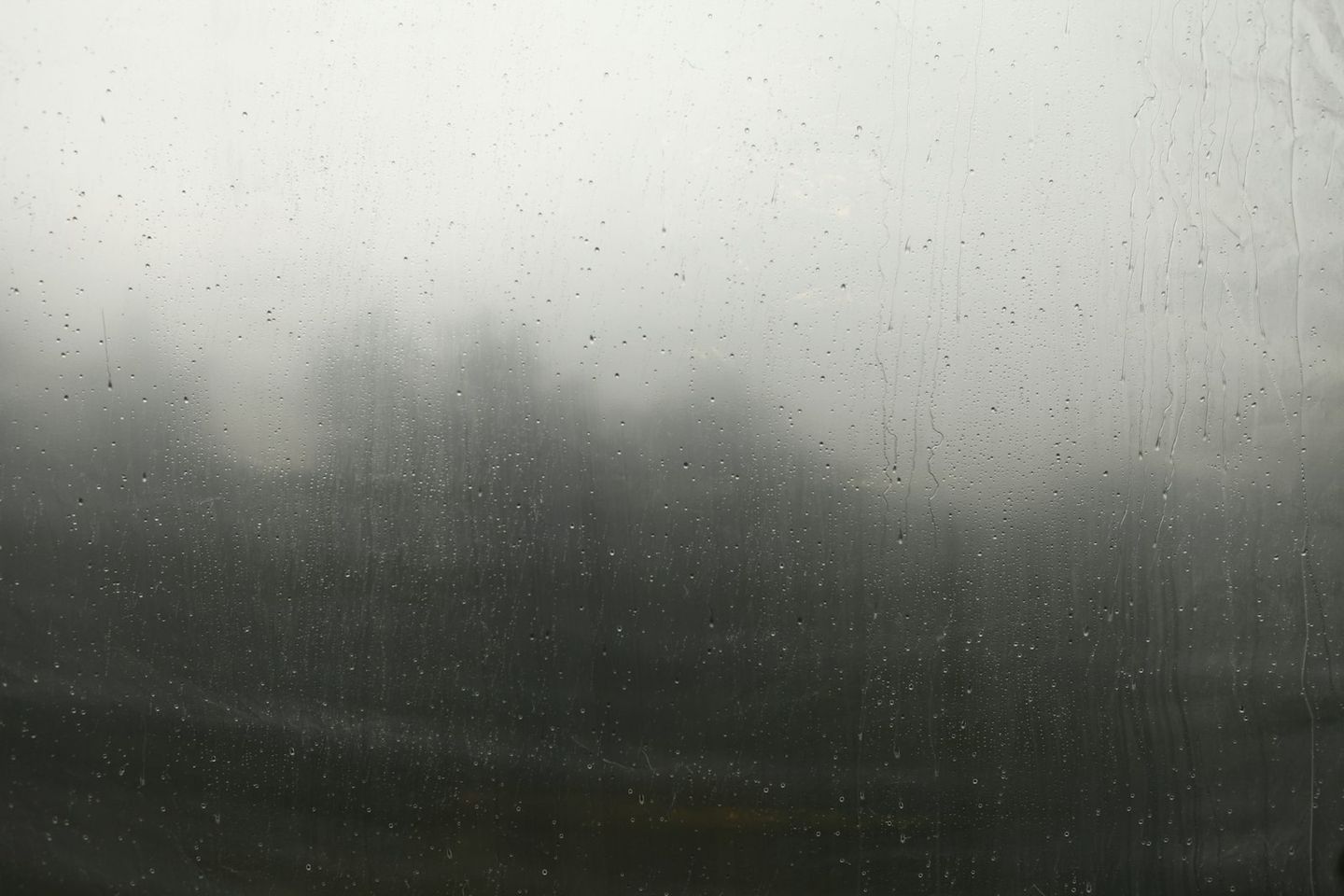 Ventana con gotas de lluvia y un paisaje neblinoso de fondo